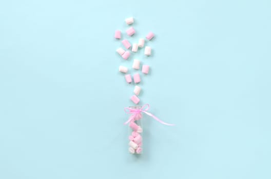Pink and white marshmallow pieces is sprayed from a small glass container on a pastel blue background. Flat lay minimalism. Top view