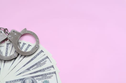 Police handcuffs and hundreds of us dollars lie on a background of living coral color. The concept of punishment for breaking the law in financial transactions