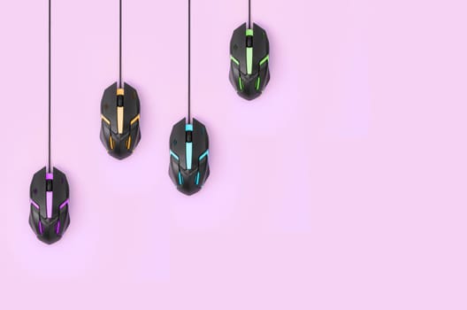 Several computer mice hang on a pastel pink background. The concept of cooperative computer video games, the use of auto-clicker and pay-per-click platforms. Flat lay with copy space