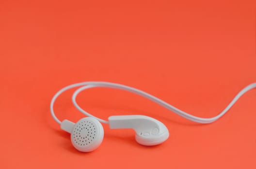 White modern headphones lie on a bright red background. A template for music listening fans
