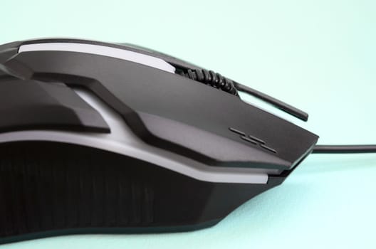 Closeup of a black gaming optical mouse on a blue background. Device for cybersport and online video games