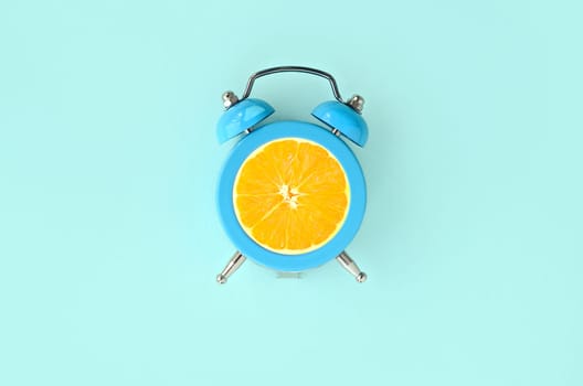Creative idea fresh orange slice alarm clock on pastel blue background. Minimal business concept. Fruit idea creative to produce work within advertising marketing solutions