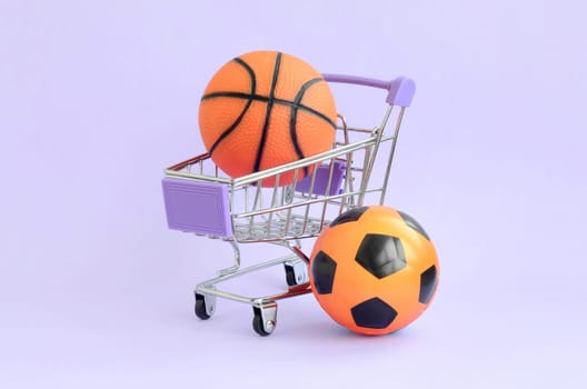 Orange basketball and soccer ball in shopping cart on violet. The concept of selling sports equipment, predictions for sports matches, sports betting