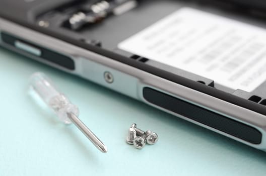 A small screwdriver and a few screws on a blue background. Tools for the repair and disassembly of modern smartphones and mobile devices
