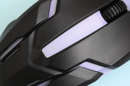 Closeup of a black gaming optical mouse on a blue background. Device for cybersport and online video games