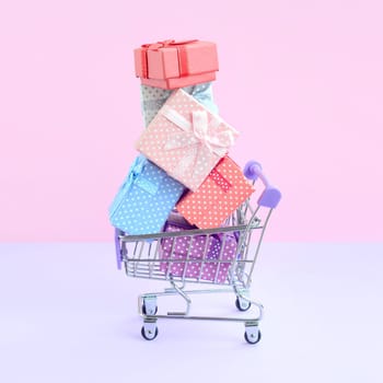 Many colorful present boxes in supermarket shopping cart on violet background. Gifts for winter holidays