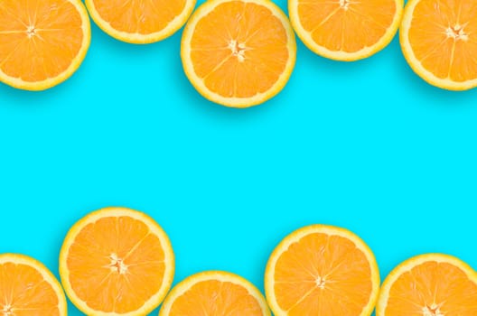 Top view of a orange fruit slices on bright blue background. A saturated citrus frame with horizontal borders. Minimalistic flat lay