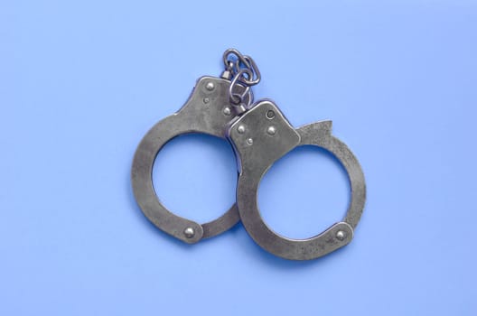 Bdsm sex games concept. Steel handcuffs lies on pastel blue background. Bondage and Discipline, Domination and Submission, Sadism and Masochism