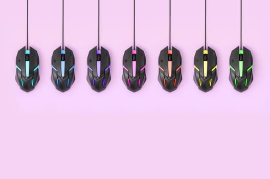 Several computer mice hang on a pastel pink background. The concept of cooperative computer video games, the use of auto-clicker and pay-per-click platforms. Flat lay abstract minimal composition