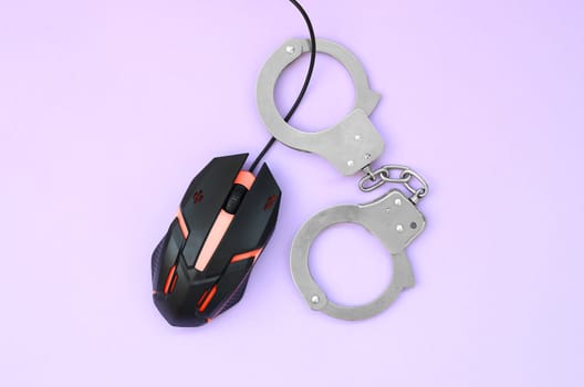 Computer mouse in a red color is chained in handcuffs on the background of purple color. The concept of combating computer crime, hackers and piracy. Flat lay top view