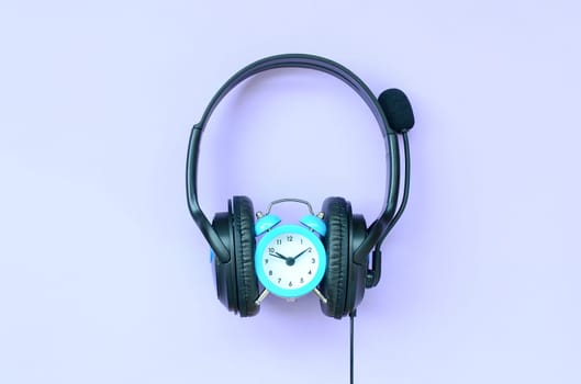 Retro alarm clock with black headphones on violet background. Concept of time to listening music
