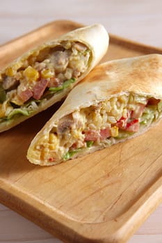 Burritos wraps with meat, beans and vegetables on wood board