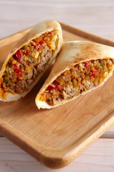 Burritos wraps with meat, beans and vegetables on wood board