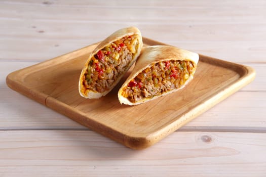 Burritos wraps with meat, beans and vegetables on wood board