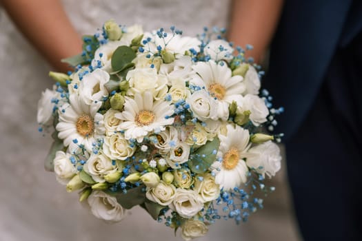 beautiful wedding bouquet in the hands of the bride on the background of a white dress