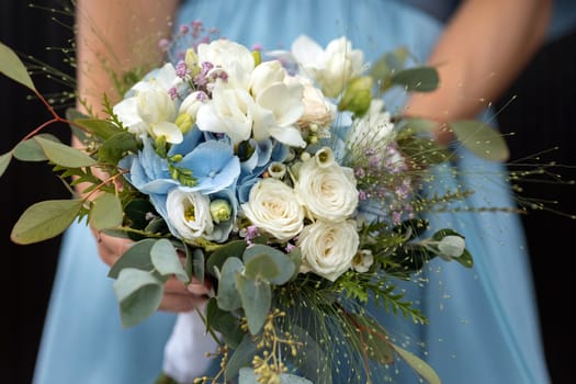beautiful wedding bouquet in the hands of the bride on the background of a blue dress