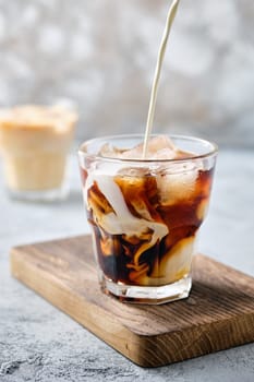 Pouring cream in iced coffee in rocks glass