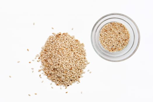 Top view of sesame seeds in a little dish and spilled on white background