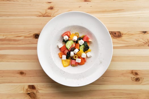Salad with pepper, tomato, cucumber, olives and feta on wooden table