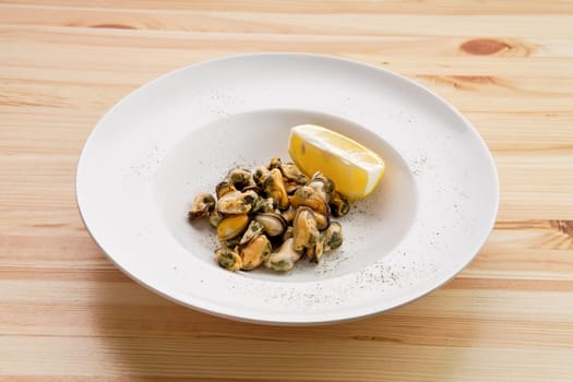 Plate with marinated mussels and slice of lemon on wooden table