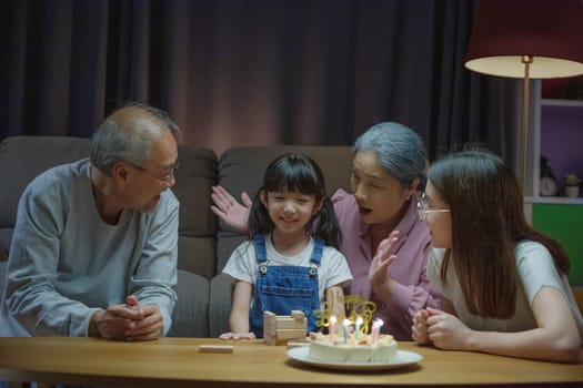 Birthday surprise. Happy Asian family grandparents and mother celebrating enjoy birthday party with cake of granddaughter at home in night time