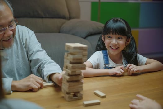Happy grandparents Asian family enjoy playing toy block with little daughter and mother together at home night time, Smiling parent having fun play build constructor tower of wooden blocks, education