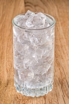 Glass of cold water with ice on wooden table, close up view