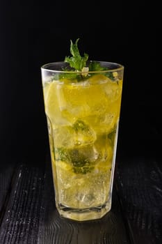 Faceted glass with cold citrus lemonade on dark wooden background