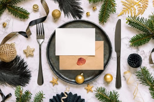 Black and golden Table setting with ornaments and fir tree branches top view, invitation card mockup. Christmas or New Year atmospheric composition on marble table, copy space.