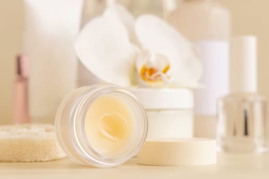 Smass opened Glass jar and other cosmetics near white orchid flower on light beige close up. Beauty products for everyday woman face care routine, Exotic Spa Treatments