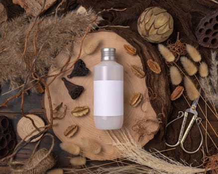 Bottle blank label on wood near natural boho decorations top view, cosmetic package mockup. Eco friendly skincare product, lotion or cream. Bohemian flat lay with dried leaves and flowers.