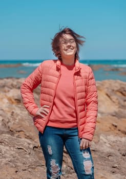 Happy Teen girl wearing pink shirt and pudded jucket, mockup. Teenager standing outdoor near the sea in a sunny day, spending her time alone. Adolescence concept