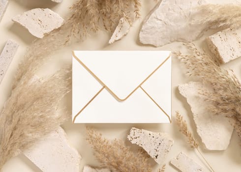 Blank horizontal envelope near beige travertine stones and boho dried pampas grass top view, mockup. Bohemian greeting or wedding Invitation. Close to nature.