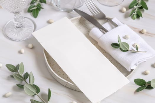 Elegant Table setting with a blank card decorated with eucalyptus branches close up, Wedding Mockup. Romantic table with paper menu card. Close to nature and simplicity concepts