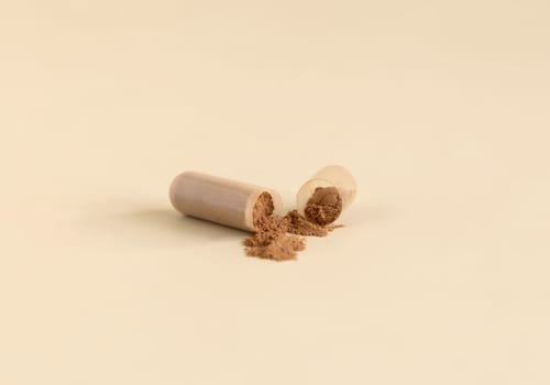 Medical capsule opened to show brown powder on light beige close up. Preventive medicine and healthcare, taking dietary supplements and vitamins. Pharmaceutical product