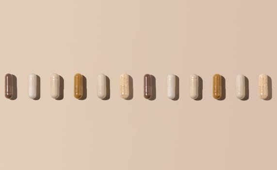 Mix of medical capsules in a line on light beige top view, hard shadows. Preventive medicine and healthcare, dietary supplements and vitamins. Assorted pharmaceutical medicine capsules