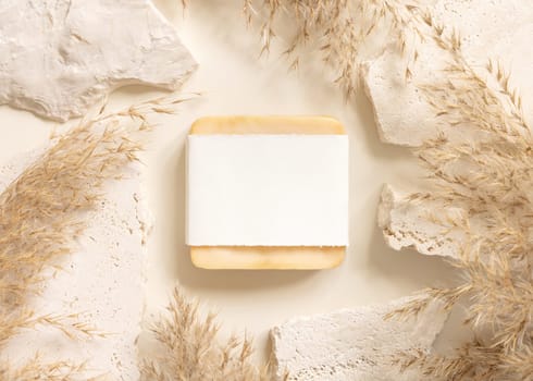 Soap bar with blank label near beige travertine stones and dried pampas grass top view, mockup. Boho scene handmade soap. Bohemian or close to nature .