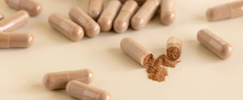 Medical capsules on light beige close up. One capsule opened to show brown powder. Preventive medicine and healthcare, taking dietary supplements and vitamins. Pharmaceutical product