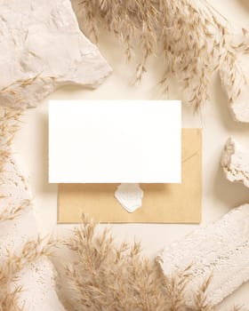 Blank card and enveelope near beige travertine stones and dried pampas grass top view, mockup. Boho scene with horizontal card. Bohemian or close to nature greeting or wedding Invitation.