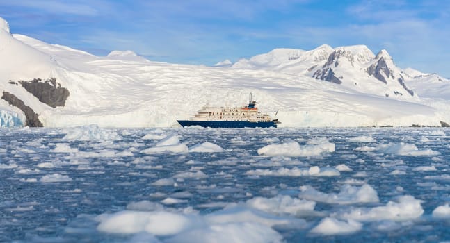 a Blue expedition ship in front of Antarctic iceberg landscape in Cierva Cove - a deep inlet on the west side of the Antarctic Peninsula, surrounded by dramatic glacier fronts