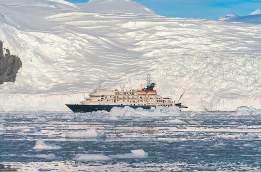 a Blue expedition ship in front of Antarctic iceberg landscape in Cierva Cove - a deep inlet on the west side of the Antarctic Peninsula, surrounded by dramatic glacier fronts