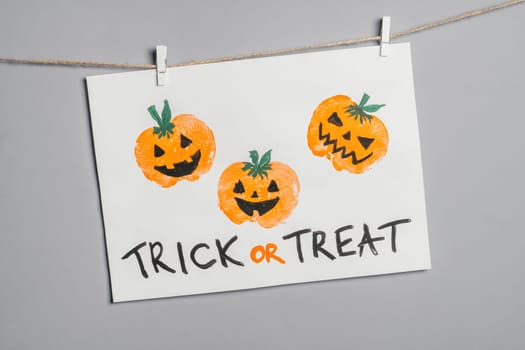 Halloween childrens pumpkin apple prints drawing hanging on rope on gray wall with Trick or Treat inscription. Handmade DIY decoration with children for holiday