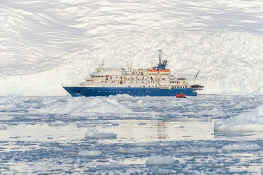 a Blue expedition ship in front of Antarctic iceberg landscape in Cierva Cove - a deep inlet on the west side of the Antarctic Peninsula, surrounded by dramatic glacier fronts