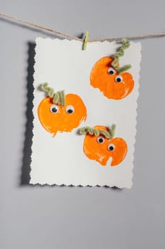 Halloween childrens pumpkin apple prints drawing hanging on rope on gray wall. Handmade DIY decoration with children for holiday. Vertical