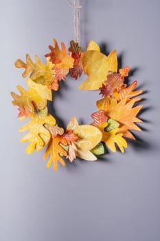 Homemade autumn yellow-red paper wreath on a gray wall background. Seasonal DIY. Vertical
