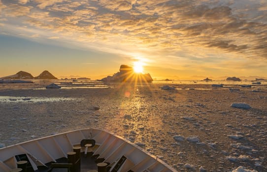 Cruise ship sails through wintry Cierva Cove - a deep inlet on the west side of the Antarctic Peninsula, ringed by Cierva Bay in San Martín Land - Antarctica, during a dramatic sunset / evening sunset.