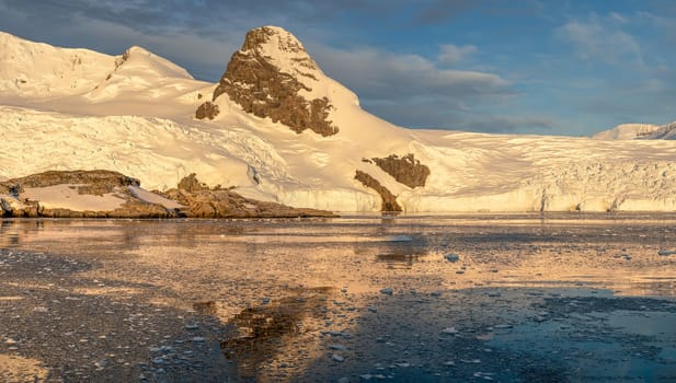 Cruise ship sails through wintry Cierva Cove - a deep inlet on the west side of the Antarctic Peninsula, ringed by Cierva Bay in San Martín Land - Antarctica, during a dramatic sunset / evening sunset.