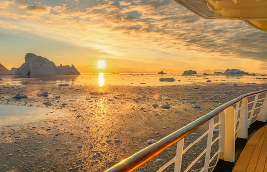 Cruise ship sails through wintry Cierva Cove - a deep inlet on the west side of the Antarctic Peninsula, ringed by Cierva Bay in San Martín Land - Antarctica, during a dramatic sunset / evening sunset.