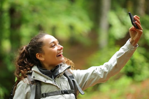 Happy hiker standing in a forest taking selfie with phone