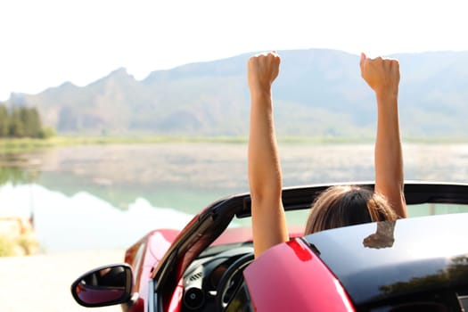 Back view portrait of a driver celebrating rsising arms in a convertible car